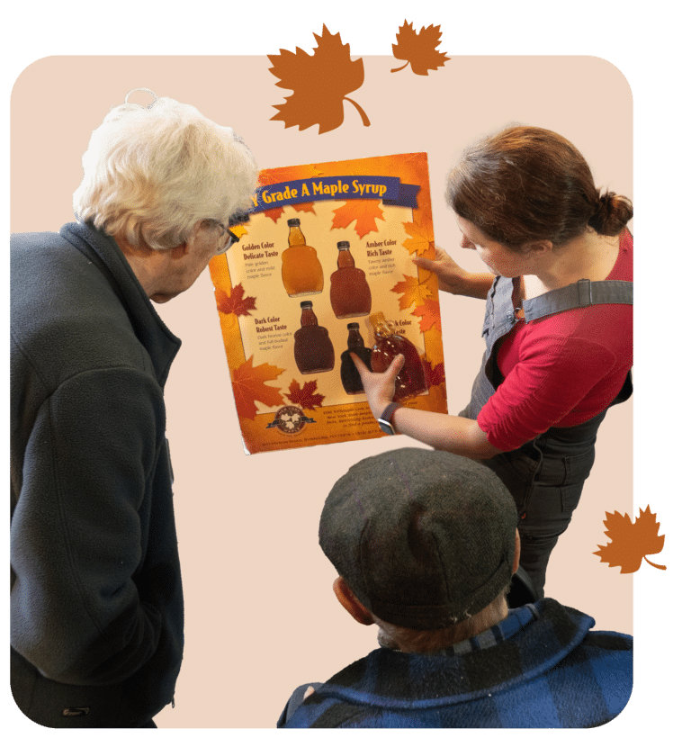 A group of three individuals look at a poster that compares the various types of New York maple syrup